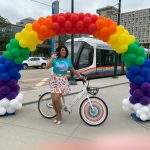 Drag queen Luna Flare with a RideKCBike under a rainbow arch 