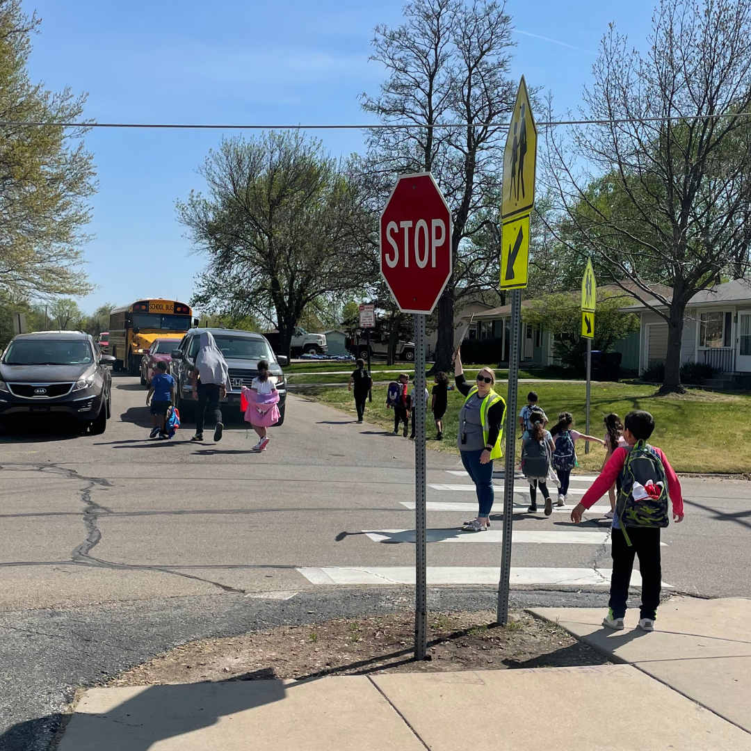 Children crossing a crosswalk and walking in the street because there is no sidewalk near their school.