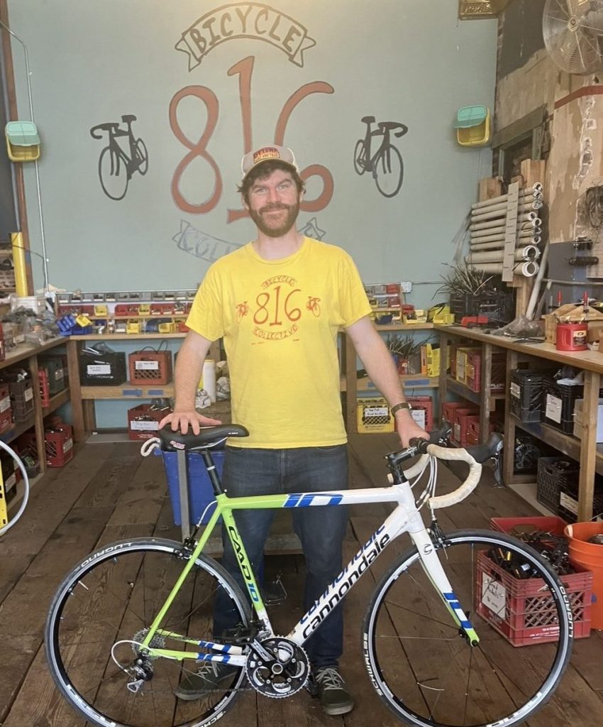 An 816 volunteer poses with a donated bike inside the 816 shop.