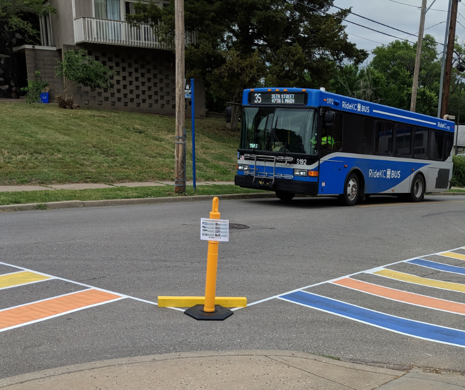 Colorful temporary crosswalks near a bus stop clearly indicate to drivers that pedestrians often cross at this intersection.